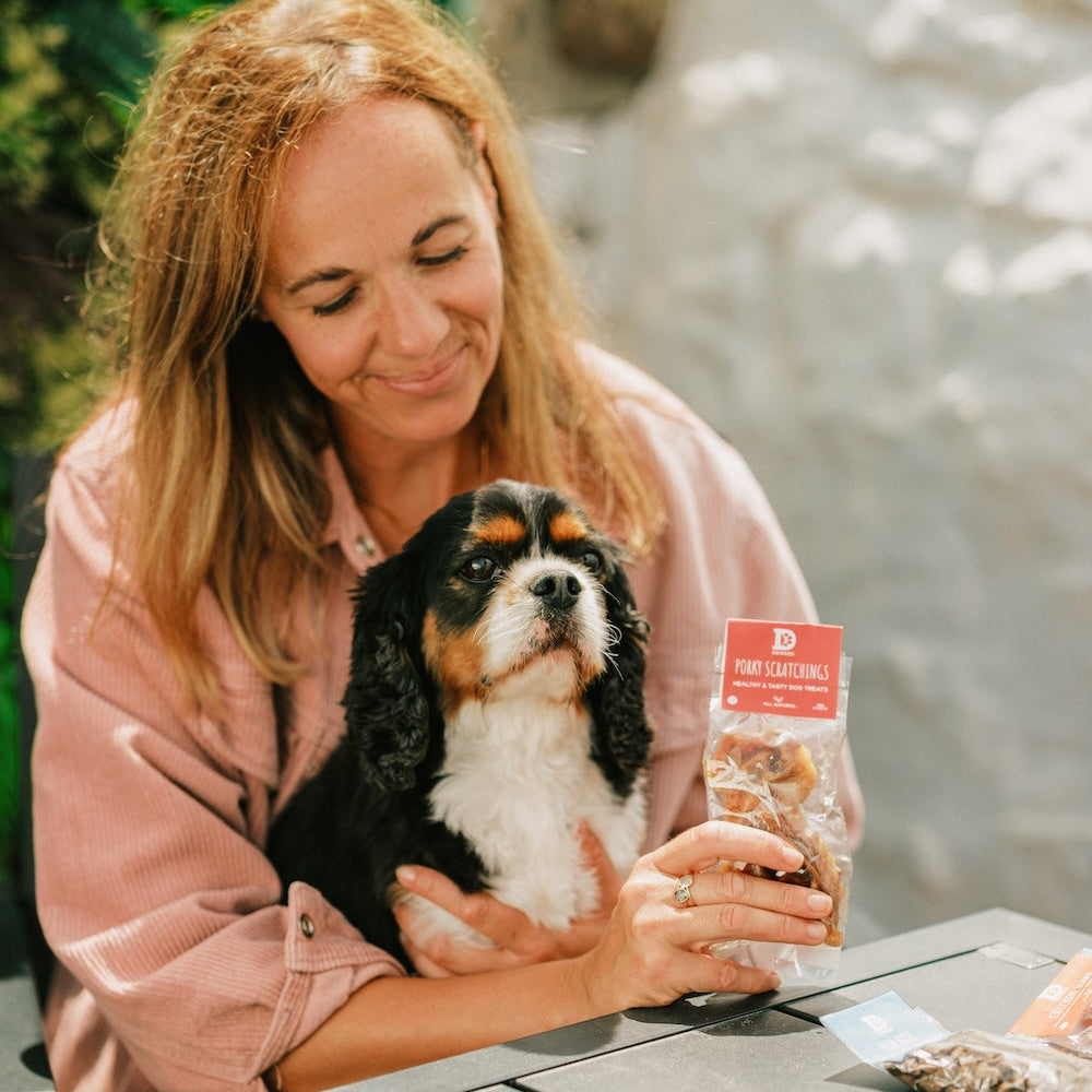 Woman holding a dog and a bag of Dewkes dog treats at an outdoor table
