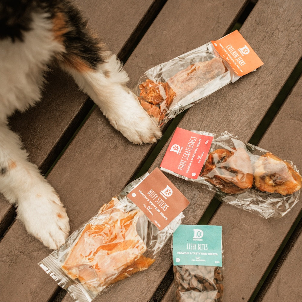 Dog pawing at packages of Dewks dog treats on a wooden surface